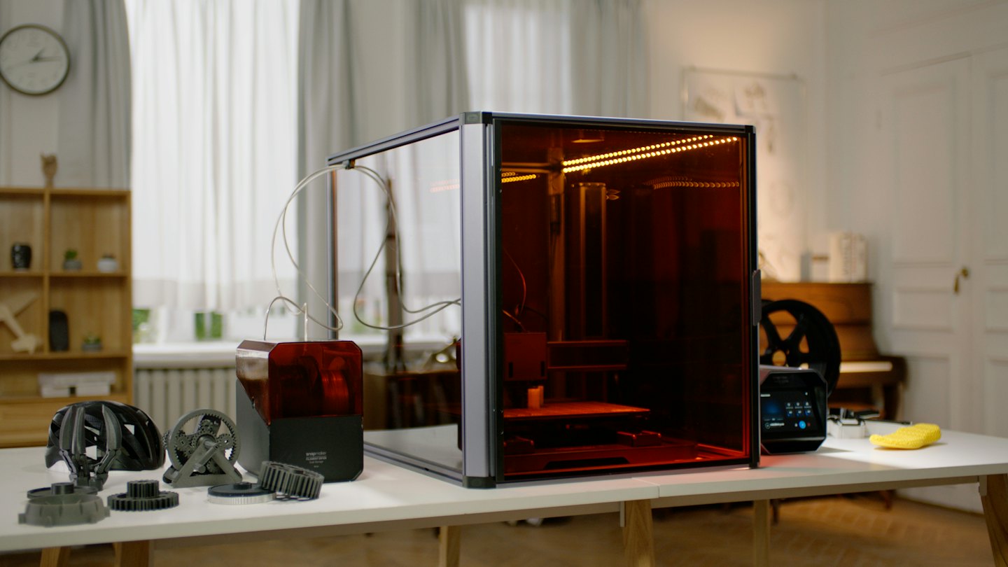 Stampante 3D con oggetti stampati su un tavolo bianco.