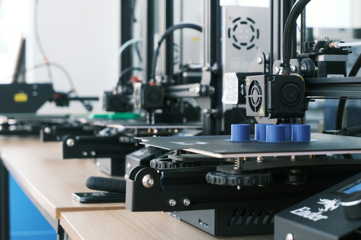 Stampanti 3D in un laboratorio che creano oggetti cilindrici blu.